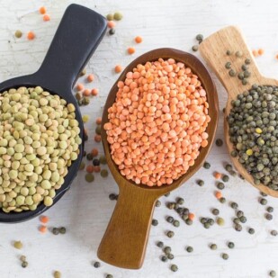 Three kinds of lentils in wooden scoops, on a white painted wooden surface