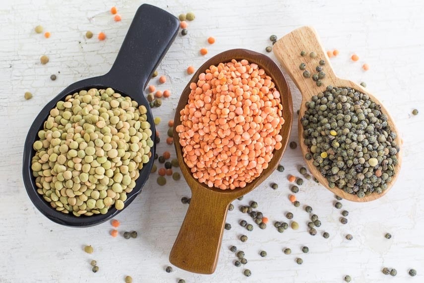 Three kinds of lentils in wooden scoops, on a white painted wooden surface