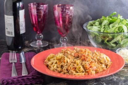 a steaming hot bowl of low FODMAP Bolognese on tagliatelle pasta; salad in background