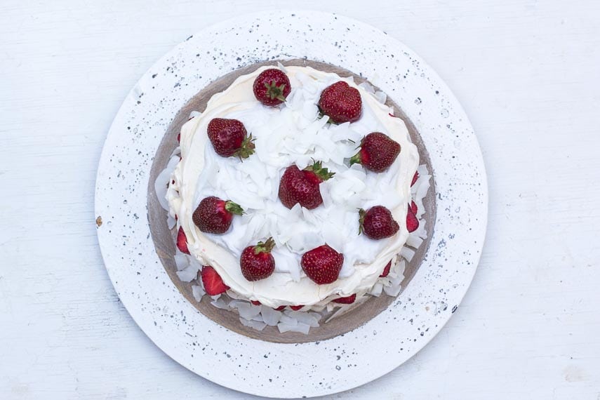 overhead image of Low FODMAP Strawberry Coconut Meringue Cake on white wooden plate against white painted wooden surface