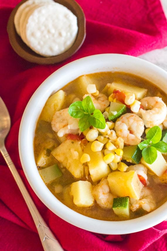 Low FODMAP Shrimp & Corn Chowder in a white bowl; red napkin and spoon and crackers alongside; vertical image