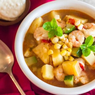 Low FODMAP Shrimp & Corn Chowder in white bowl; crackers and spoon alongside