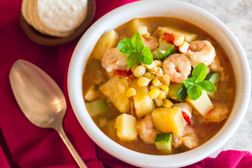 Low FODMAP Shrimp & Corn Chowder in white bowl; crackers and spoon alongside