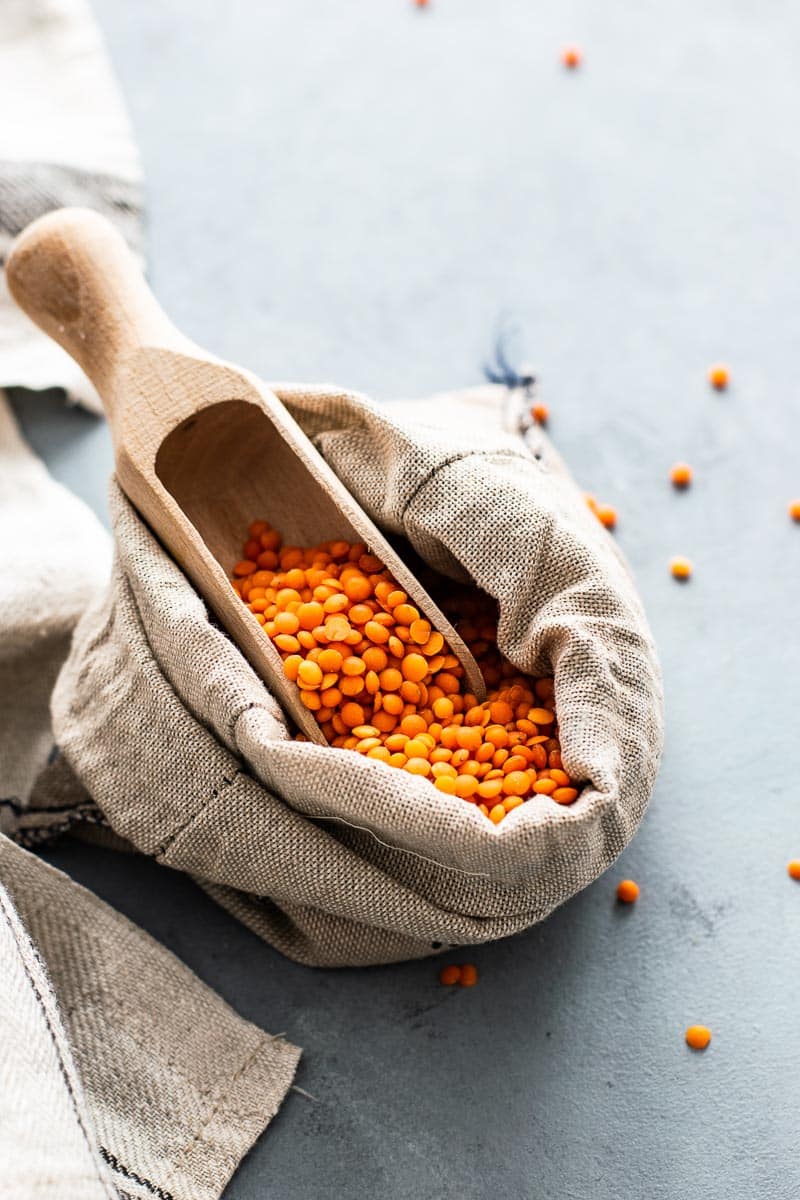 red lentils in a wooden scoop against light background
