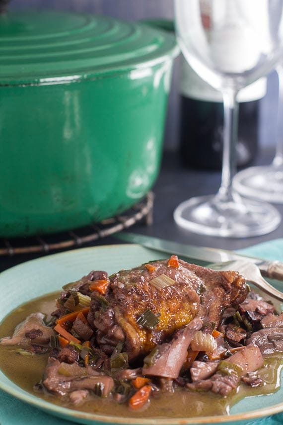 vertical image of coq au vin with green pot and wine glasses in background