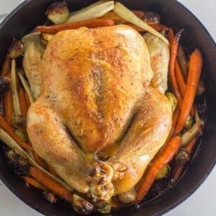Low FODMAP whole roast chicken and vegetables in cast iron pan on white quartz