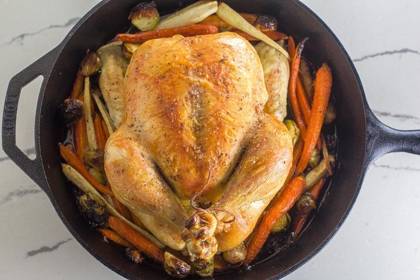 Low FODMAP whole roast chicken and vegetables in cast iron pan on white quartz