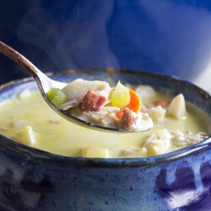 closeup of low FODMAP fish chowder on spoon and in rustic blue bowl