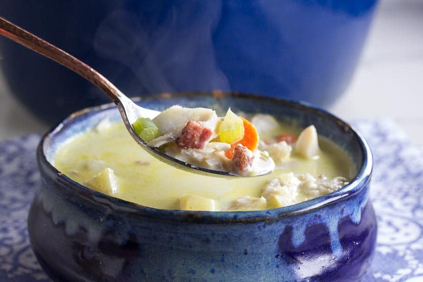 closeup of low FODMAP fish chowder on spoon and in rustic blue bowl