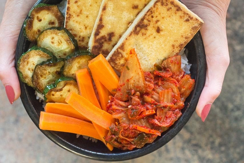 hands holding bowl of rice, tofu, zucchini, carrot and low FODMAP kimchi