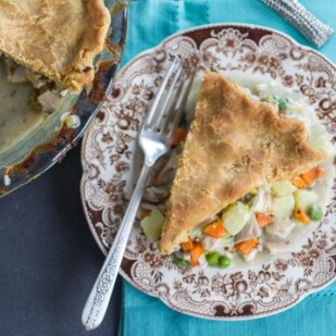 overhead image of Low FODMAP CHicken Pot Pie slice on brown decorative plate on teal cloth; whole pie alongside