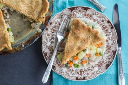 overhead image of Low FODMAP CHicken Pot Pie slice on brown decorative plate on teal cloth; whole pie alongside