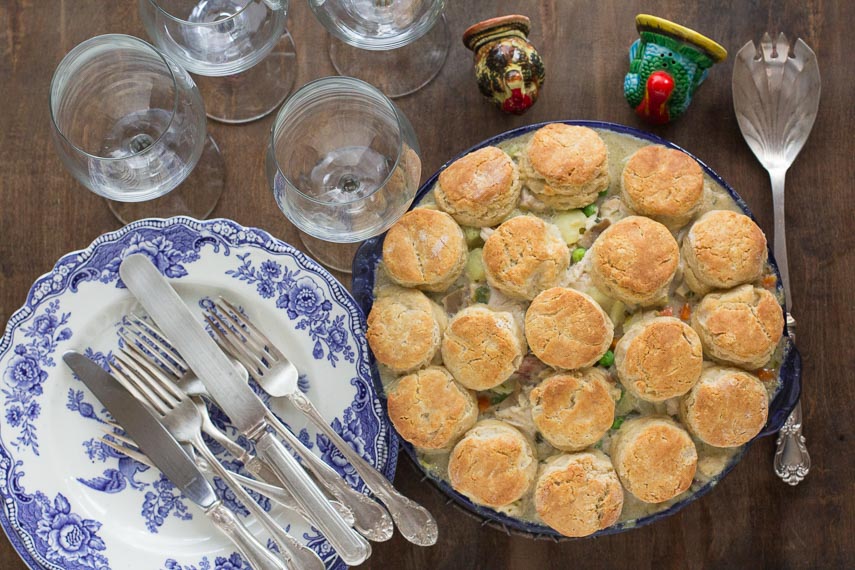 overhead image of Low FODMAP Leftover Turkey Pot Pie with Biscuit Topping on brown wooden background; blue and white plates alongside