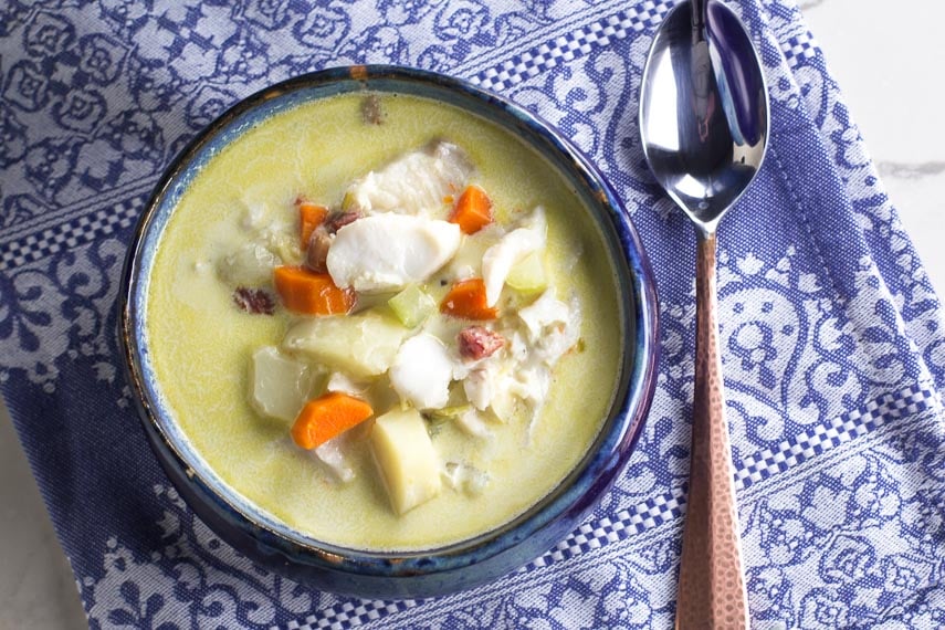 overhead of low FODMAP fish chowder in blue bowl with hammered copper spoon