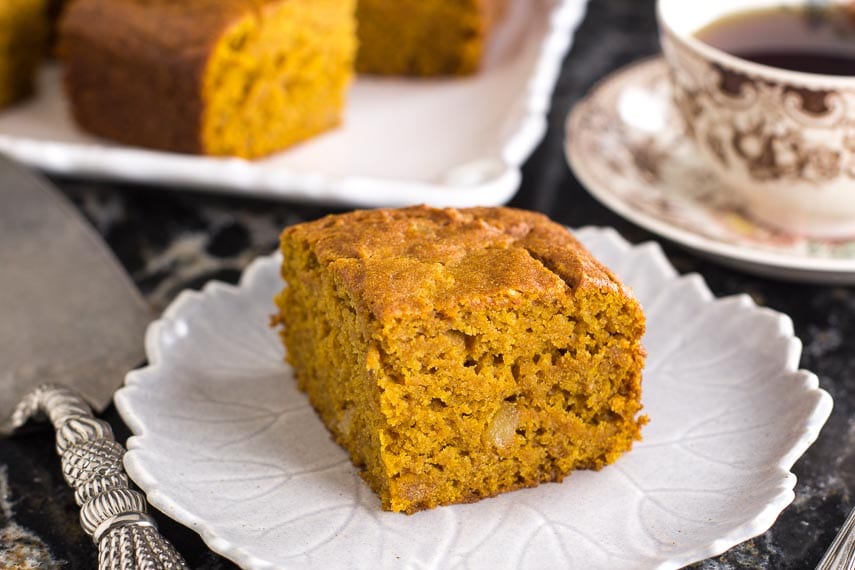 square piece of low FODMAP triple ginger pumpkin cake on white plate; coffee cup in background