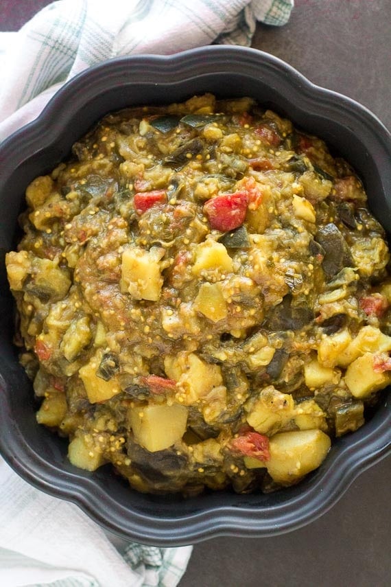 vertical image of Potato eggplant curry in black casserole dish