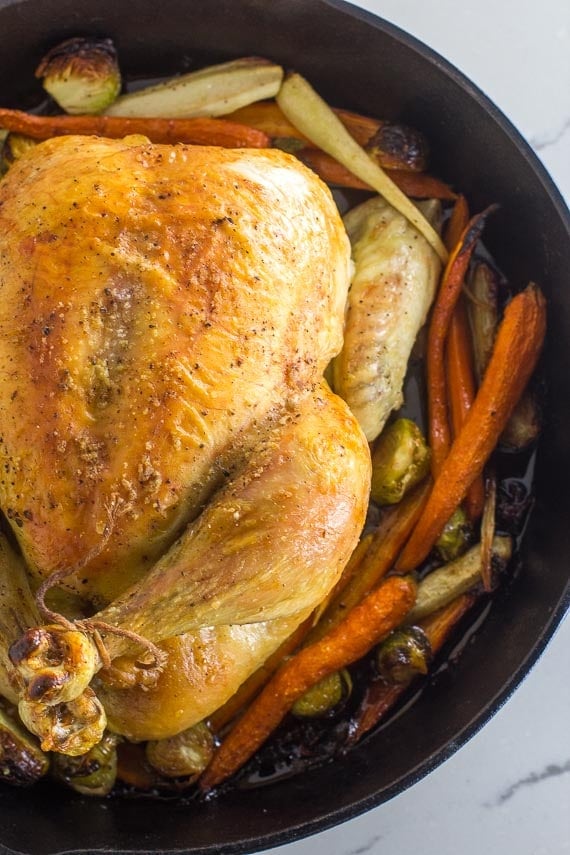 vertical whole roast chicken with vegetables in cast iron pan closeup