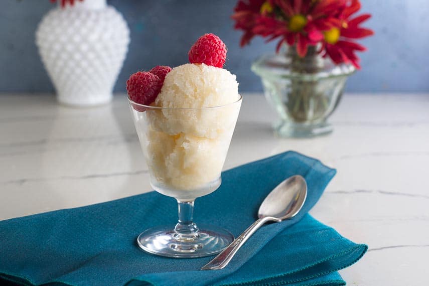 Low FODMAP lemon granita in clear glass footed dish; teal napkin underneath and silver spoon alongside