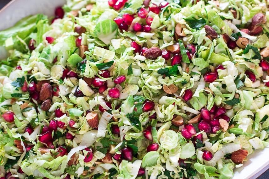 closeup of Low FODMAP Brussels sprouts salad with pomegranate and almonds on white oval platter_