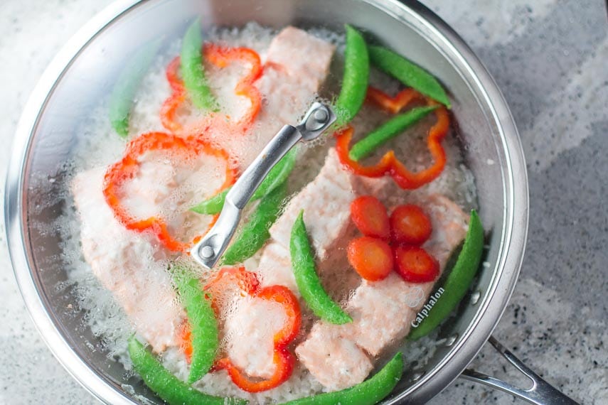 low FODMAP one-pot salmon with snow peas in skillet on gray quartz surface steaming under glass lid