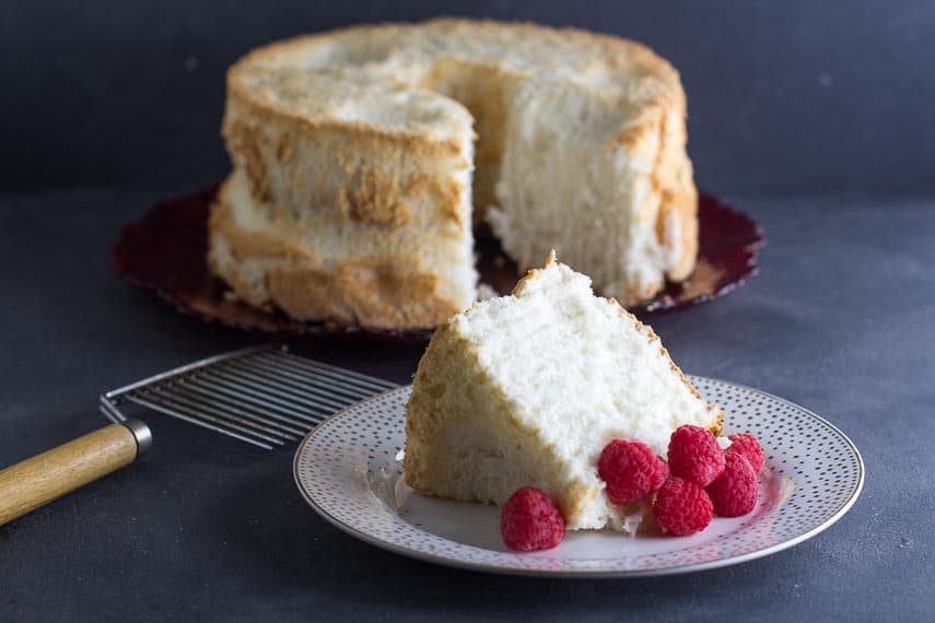 low FODMAP angel food cake in background; slice in foreground. Angel Food Cake cutter alongside