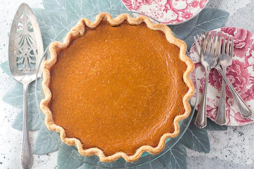 overhead image of low FODMAP classic pumpkin pie in glass pie plate with silver server