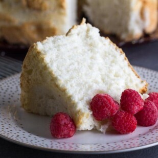 slice of low FODmAP Angel Food Cake on decorative plate with fresh raspberries