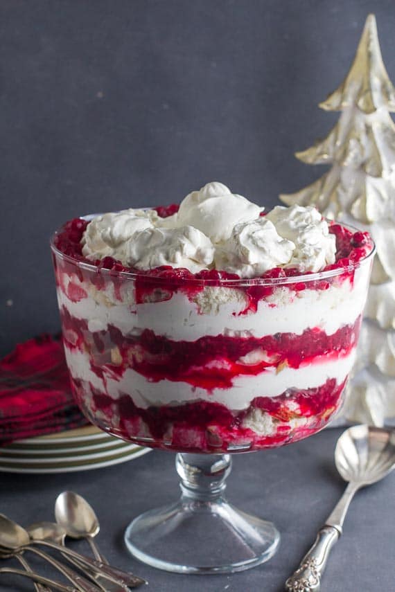 vertical image of low FODMAP Cranberry Raspberry Cheesecake Trifle in glass trifle bowl with silver serving spoon alongside