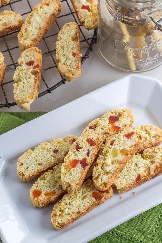 vertical image of Low FODMAP Tropical Biscotti on white plate; cooling rack with cookies in background