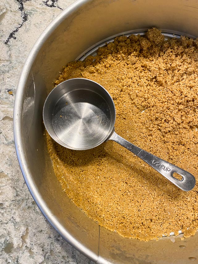 Pressing a cookie crumb crust into a springform pan, using the flat bottom of a measuring cup to help create an even layer