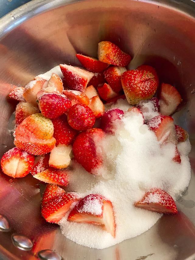 combining chopped strawberries and sugar in a nonreactive pan to make glaze for cheesecake