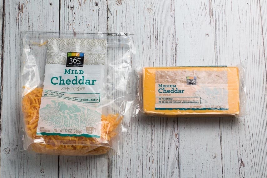 comparison of pre-shredded cheddar cheese and block cheddar cheese against white wooden backdrop