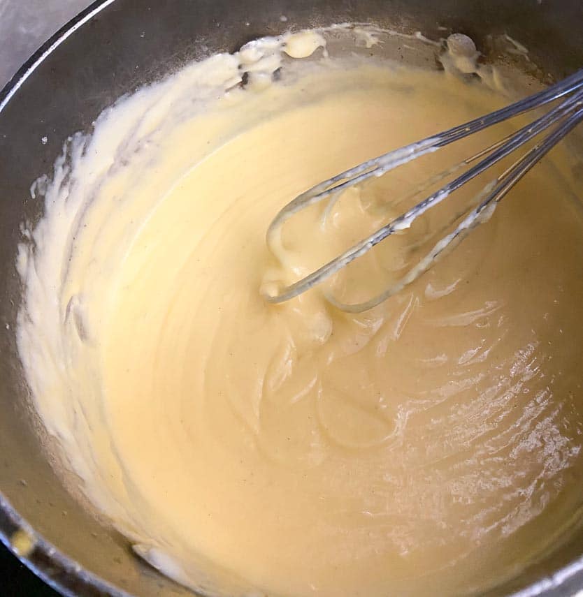 creamy cheese sauce ready for pasta in our low FODMAP Mac and cheese recipe; in pot with whisk