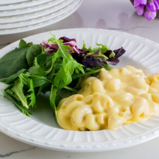 creamy mac and cheese on a white plate with salad on white counter