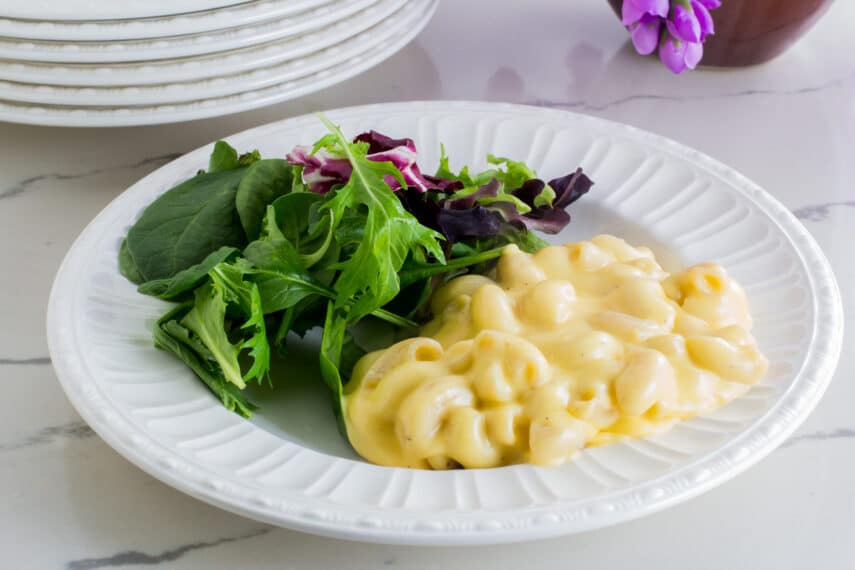 creamy mac and cheese on a white plate with salad on white counter