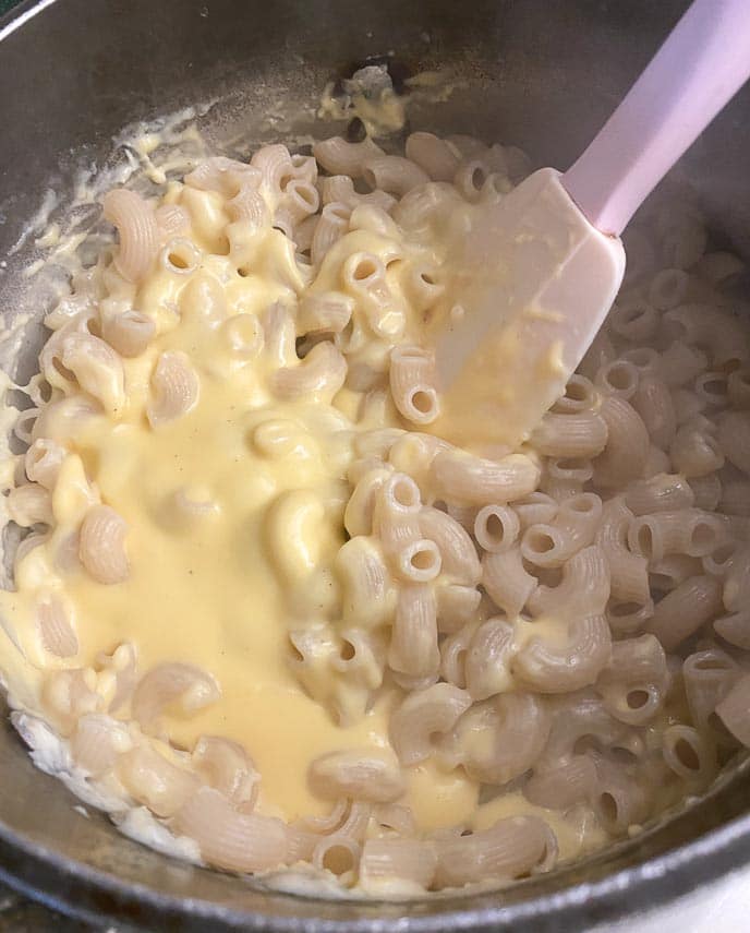 folding pasta elbows into cheese sauce for low FODMAP mac and cheese; in pot with silicone spatula