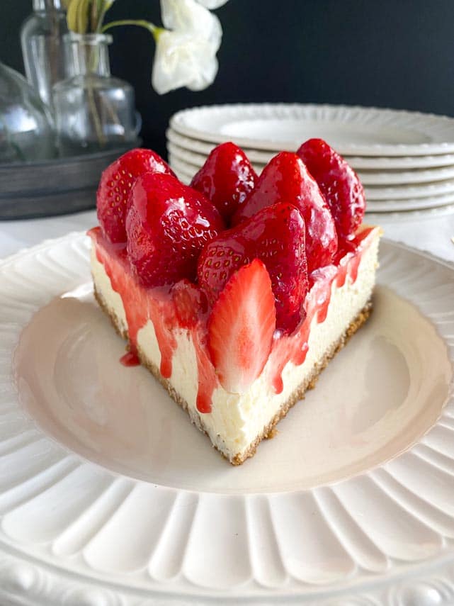 head on image of slice of strawberry glazed cheesecake on white plate