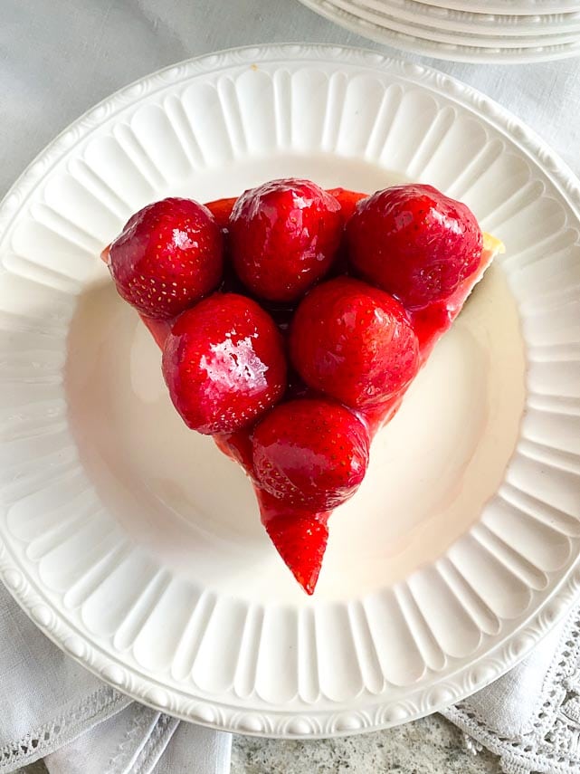 slice of strawberry glazed NY style cheesecake on decorative white plate