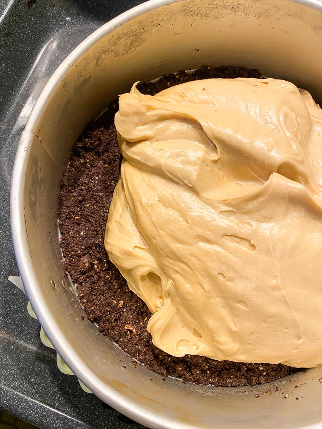 spreading peanut butter cheesecake batter on top of par-baked chocolate cookie crust in springform pan