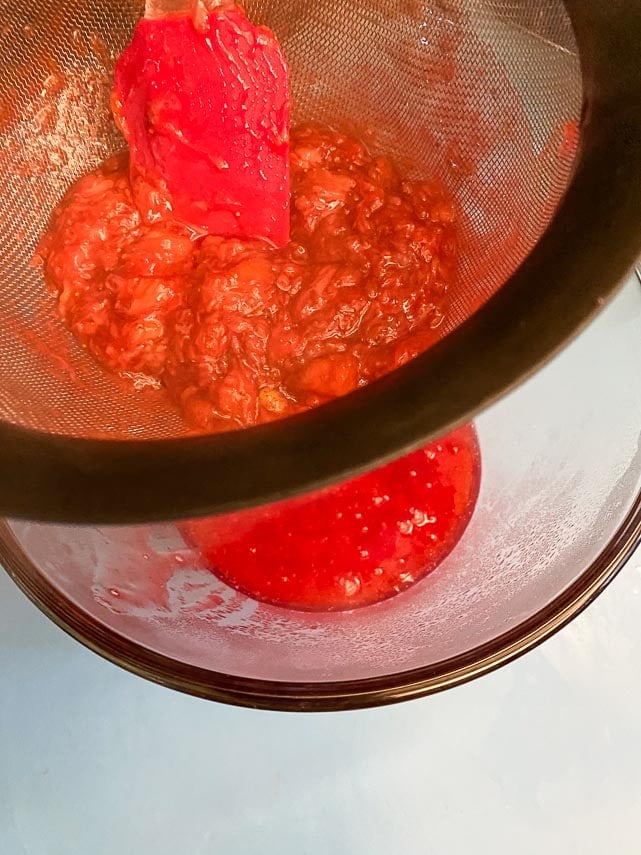 straining our berries for strawberry glaze into glass bowl