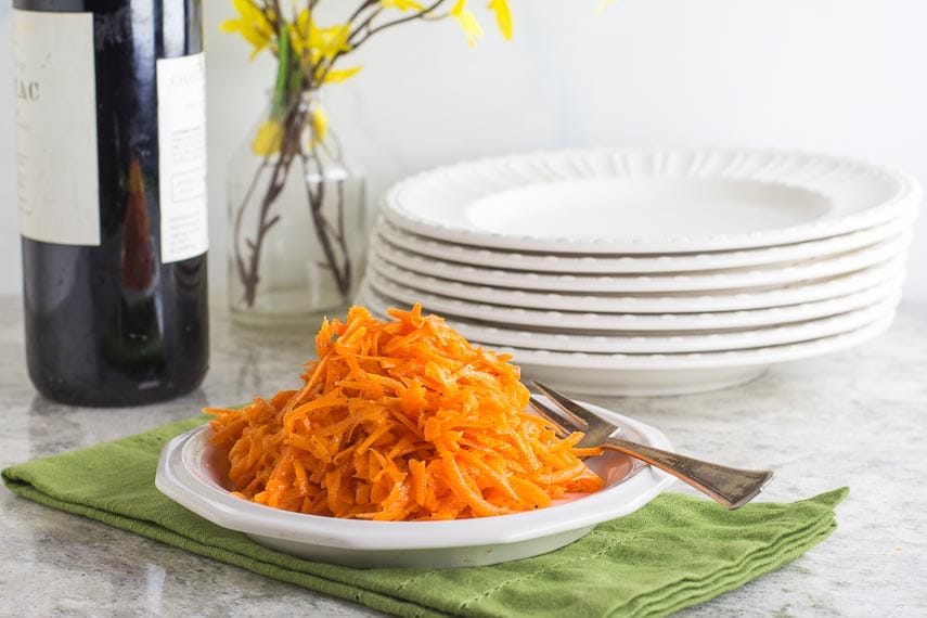 Low FODMAP Grated Carrot Salad on white plate; green napkin underneath, white plates and wine bottle alongside