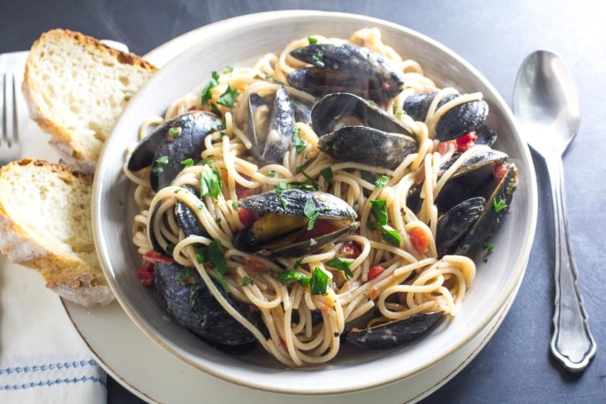 Low FODMAP Pasta with Mussels in a white bowl with bread alongside