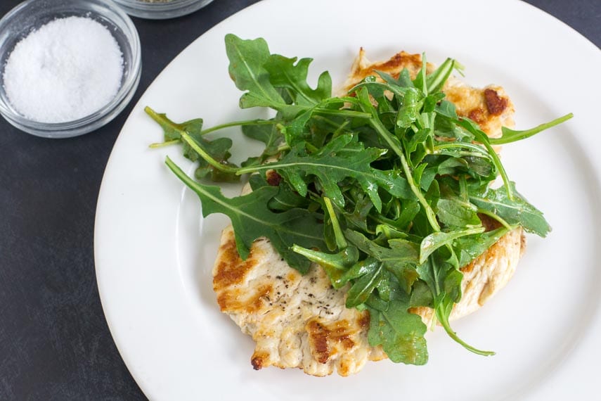 No FODMAP Chicken Paillard on white plate topped with no FODMAP arugula salad