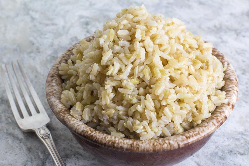 brown rice in a brown ceramic bowl with silver fork