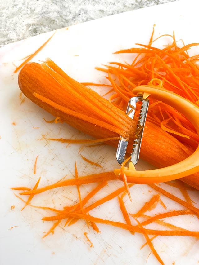 carrot being cut into julienne using a handy dandy julienne peeler. EASY! And inexpensive