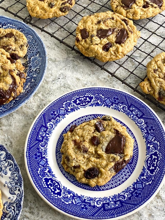 every cookie has a unique look. One-bowl low FODMAP peanut butter oatmeal chocolate chunk cookies on blue decorative plate. Cooling rack in background
