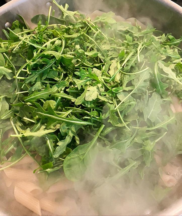 low FODMAP Pasta Primavera cooking; stirring in arugula and spinach