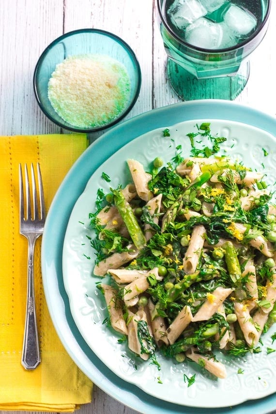 low FODMAP pasta primavera on aqua colored plates; yellow napkin and Parmesan cheese alongside