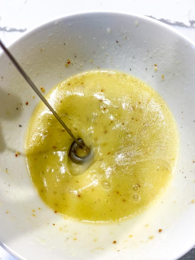 emulsifying lemon salad dressing in a white bowl with a tiny frother