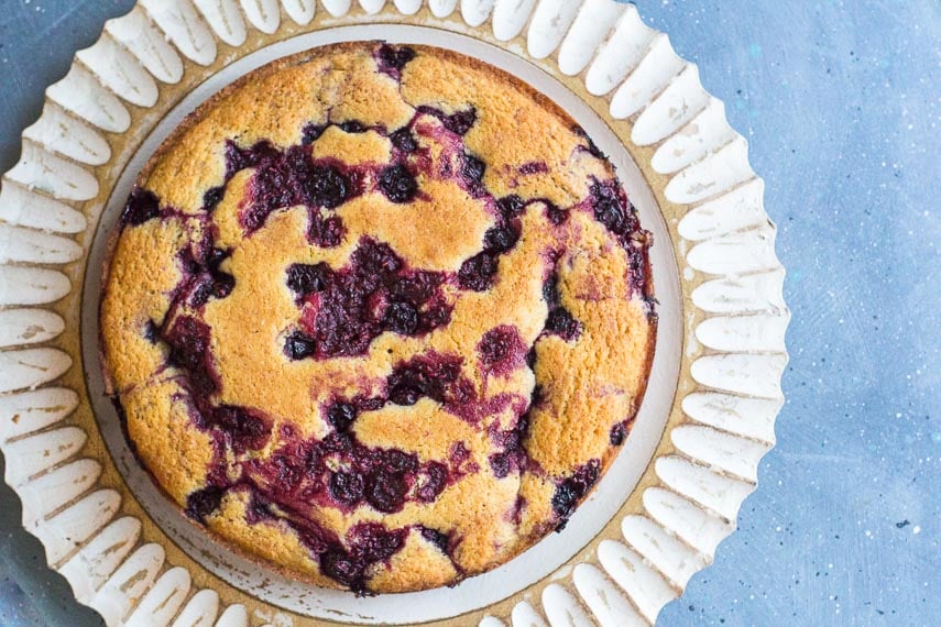 Low FODMAP Cornmeal Berry Snack cake with berries on decorative wooden plate on blue background